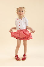 Load image into Gallery viewer, Young girl wearing a white blouse with red buttons and a pink skirt on a beige background