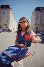 Load image into Gallery viewer, Young girl in a blue dress holding pink tulips on a city street.