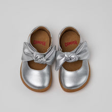 將圖片載入圖庫檢視器 A pair of metallic silver Mary Jane style baby shoes with a satin bow on the toe, shown from a top-down view on a light gray background. The brand name 'CHAMPER' is visible in red on the insole.