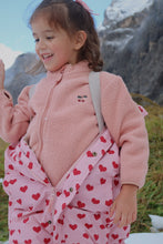 Load image into Gallery viewer, Child wearing a pink fleece jacket and red heart-patterned pants outdoors with mountains in the background