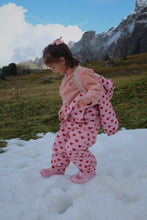 Load image into Gallery viewer, Child in pink heart-patterned outfit standing on snow with mountains in the background