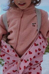 Child wearing a pink fleece jacket with heart pattern in a snowy outdoor setting