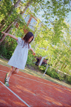Load image into Gallery viewer, Young girl in a white dress running on a track with trees in the background