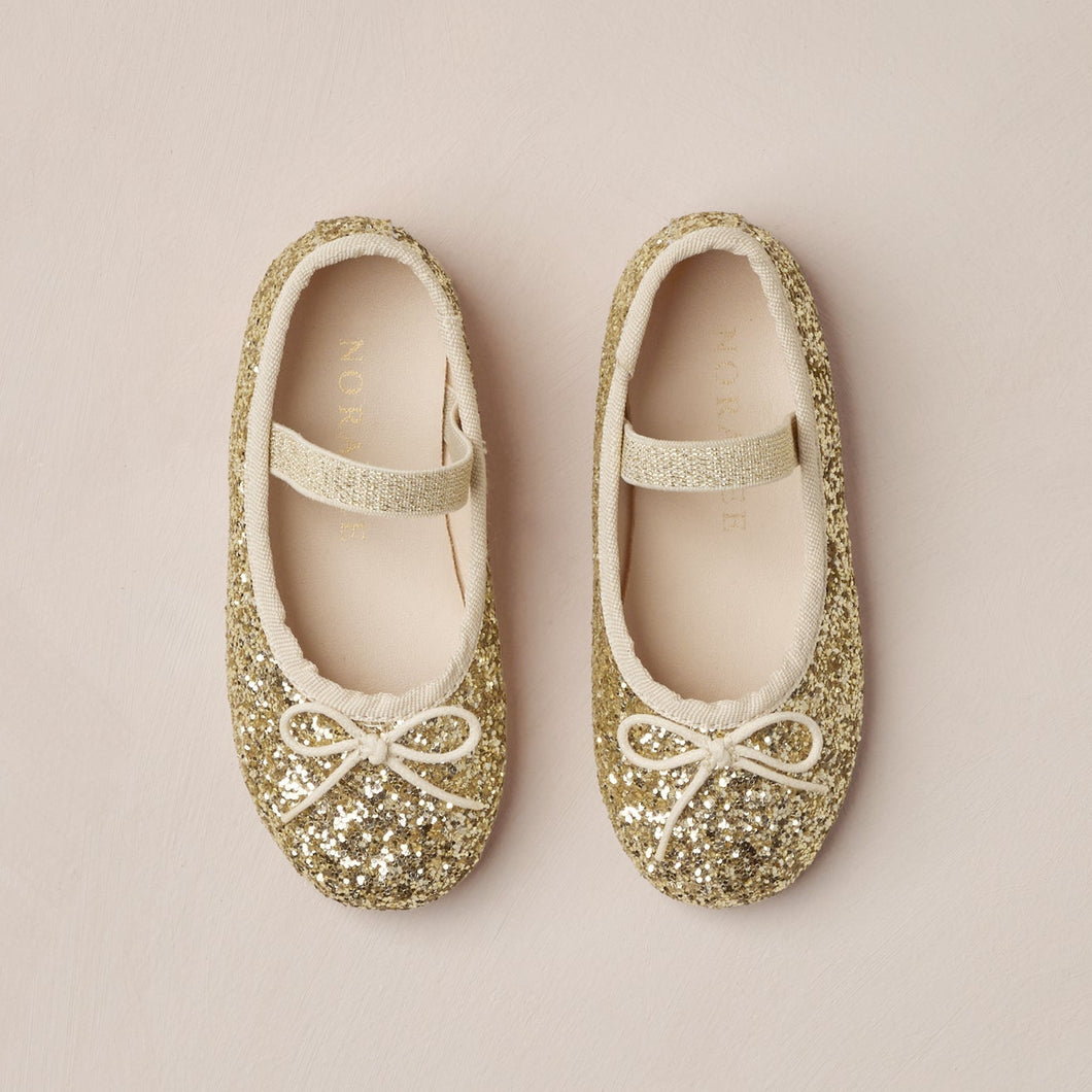 Pair of gold glittery ballet flats on a beige background