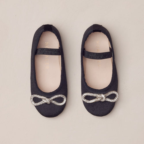 Pair of black shoes with silver bows on a beige background