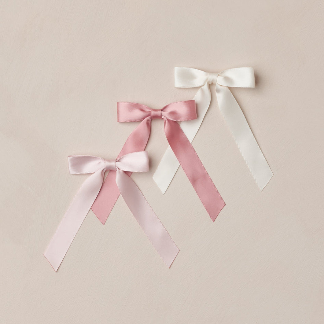 Three satin ribbons in pink, white, and light pink on a beige background