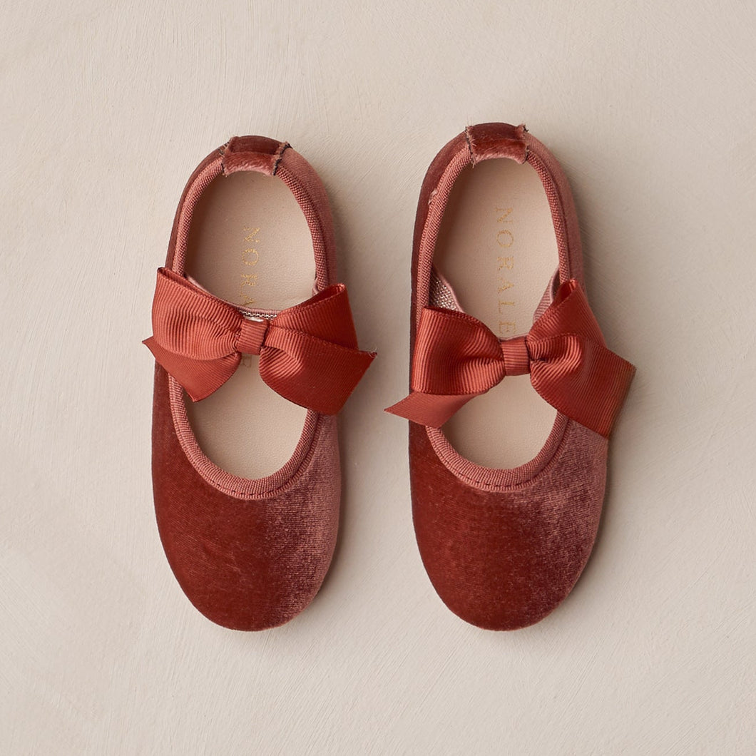 Pair of red velvet shoes with bows on a beige background
