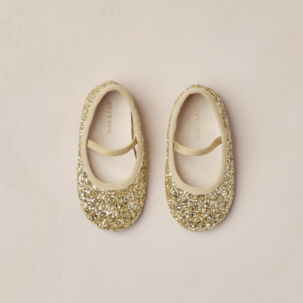 Pair of gold glittery ballet flats on a beige background