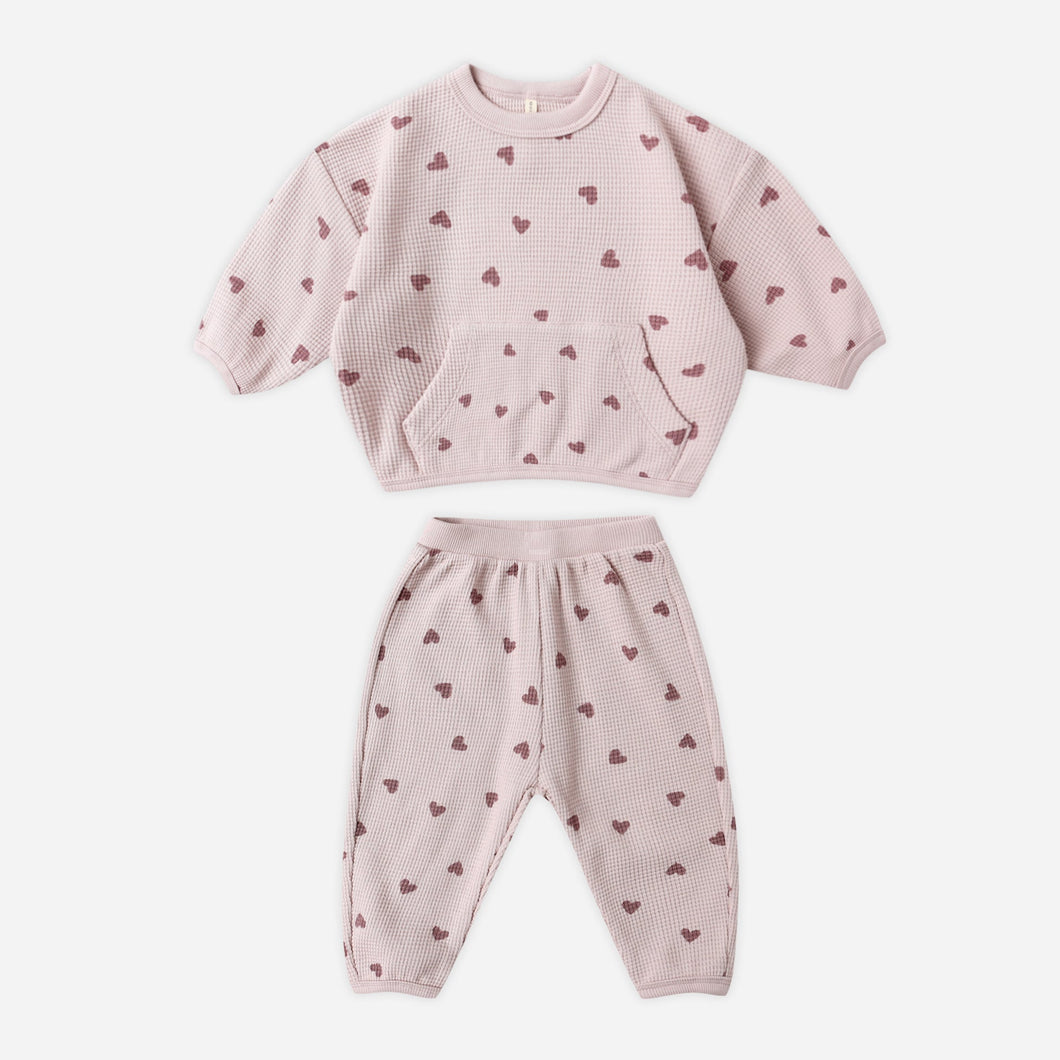 Pink children's sweatshirt and pants set with heart patterns on a white background