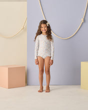 Load image into Gallery viewer, Baby girl wearing Rylee+Cru one-piece rashguard bloom swimwear, featuring a floral pattern and long sleeves for sun protection.