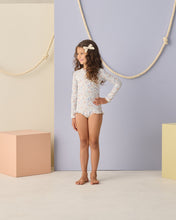 Load image into Gallery viewer, Baby girl wearing Rylee+Cru one-piece Bloom rashguard swimwear with short sleeves and floral pattern, front view.