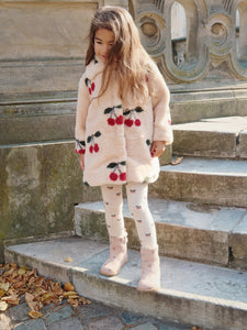 Young girl in a cherry-patterned coat standing on stone steps outdoors.