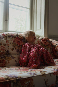 Child in a red sequin dress sitting on a floral couch by a window