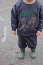 將圖片載入圖庫檢視器 Child wearing a dark gray sweatshirt with animal prints and text, standing on a paved surface.