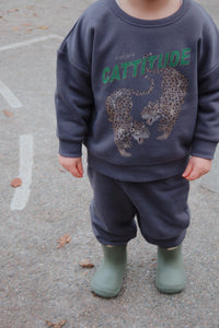 Child wearing a dark gray sweatshirt with animal prints and text, standing on a paved surface.