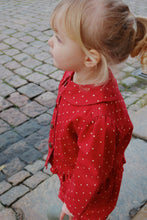 Load image into Gallery viewer, Child wearing a red polka dot dress on a cobblestone street