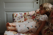 Load image into Gallery viewer, Child in a floral dress sitting on a floral-patterned couch.