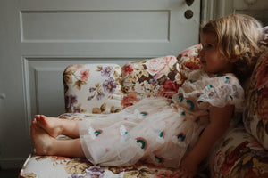 Child in a floral dress sitting on a floral-patterned couch.