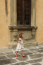 將圖片載入圖庫檢視器 Young girl in a white dress walking on a stone pavement in front of an old building.
