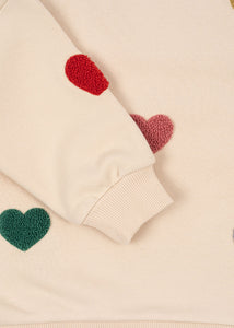 Close-up of a beige sweater with red and green heart patterns.