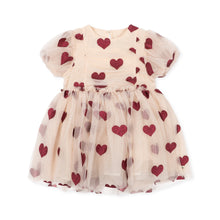 Load image into Gallery viewer, A toddler girl's tulle dress in a light beige or cream color, decorated with an all-over pattern of red and dusty rose hearts. The dress features short puff sleeves, a smocked bodice, and a tiered tulle skirt, shown flat on a white background.