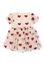 Load image into Gallery viewer, A toddler girl's tulle dress in a light peach-beige color, decorated with a pattern of dark red and dusty rose hearts. The dress features short puff sleeves and a gathered tulle skirt, shown against a plain white background.